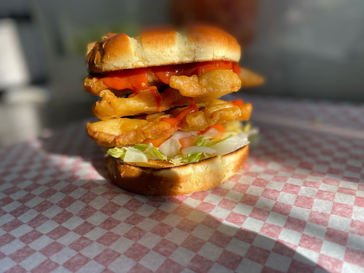 A hand breaded tenderloin sandwich with hot sauce, photographed in low sun